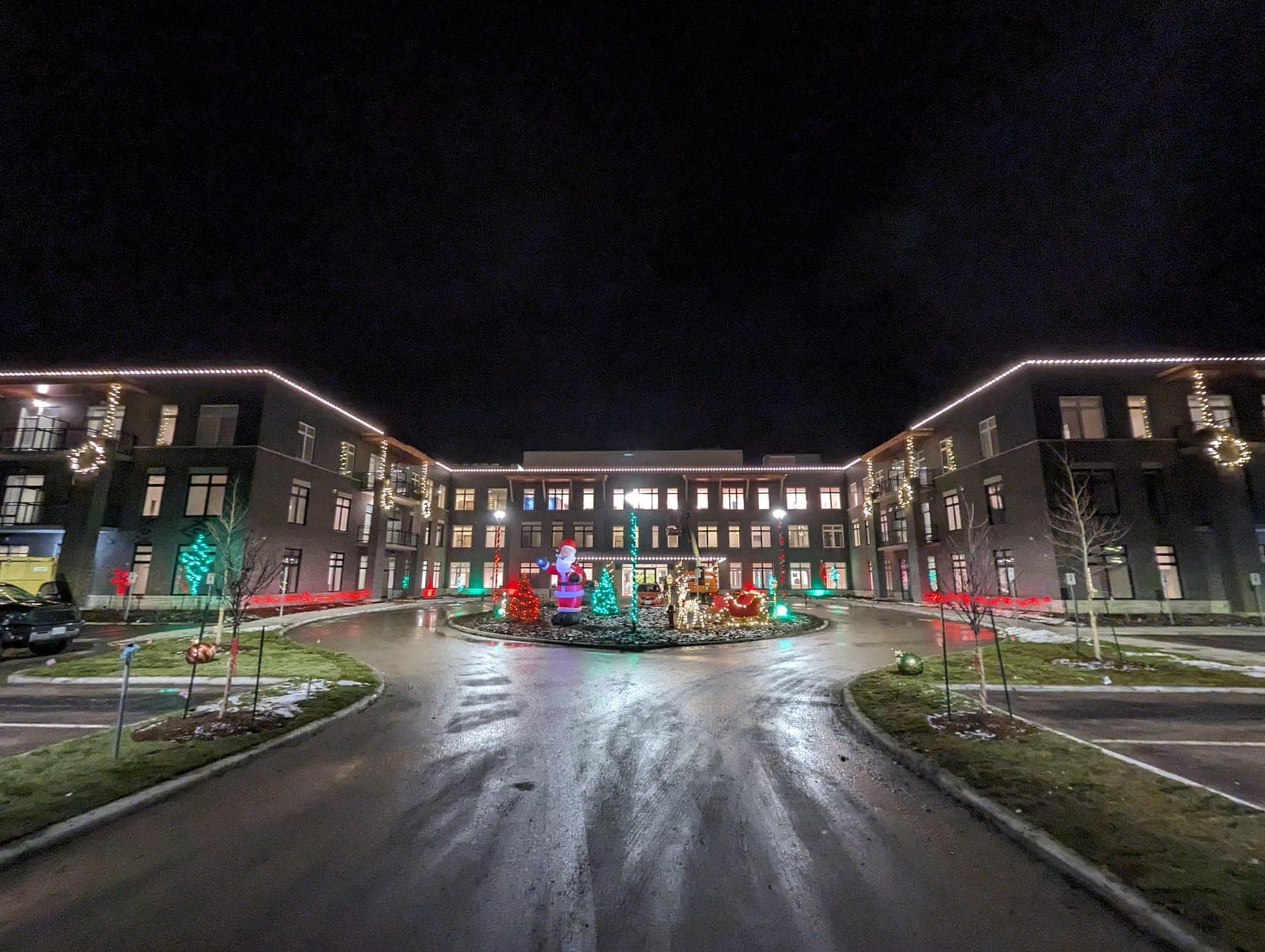 Large residential complex with warm-white roofline Christmas lights and a holiday courtyard display at the entrance