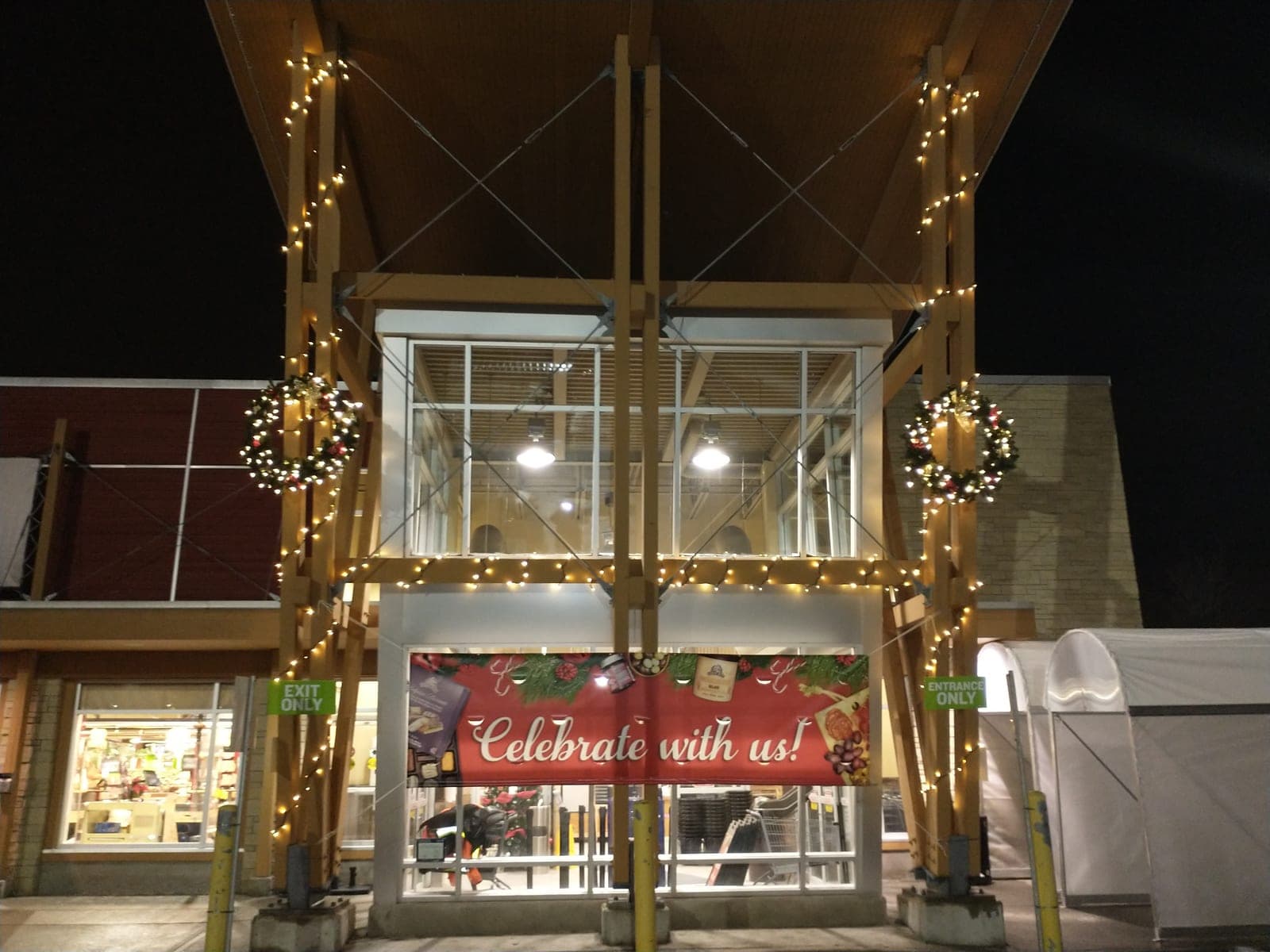 Commercial storefront entrance decorated with lit Christmas wreaths and warm white string lights at night.