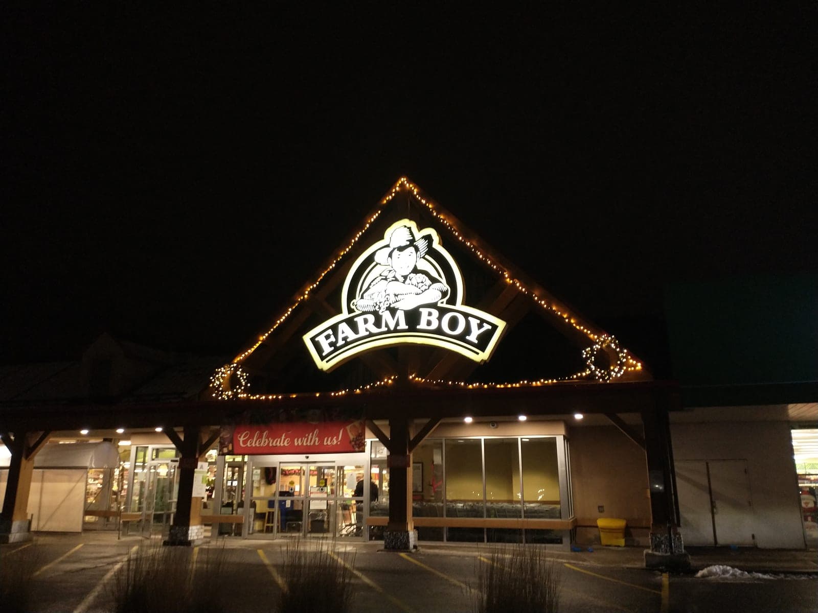 Commercial grocery storefront entrance gable trimmed with warm-white Christmas lights at night