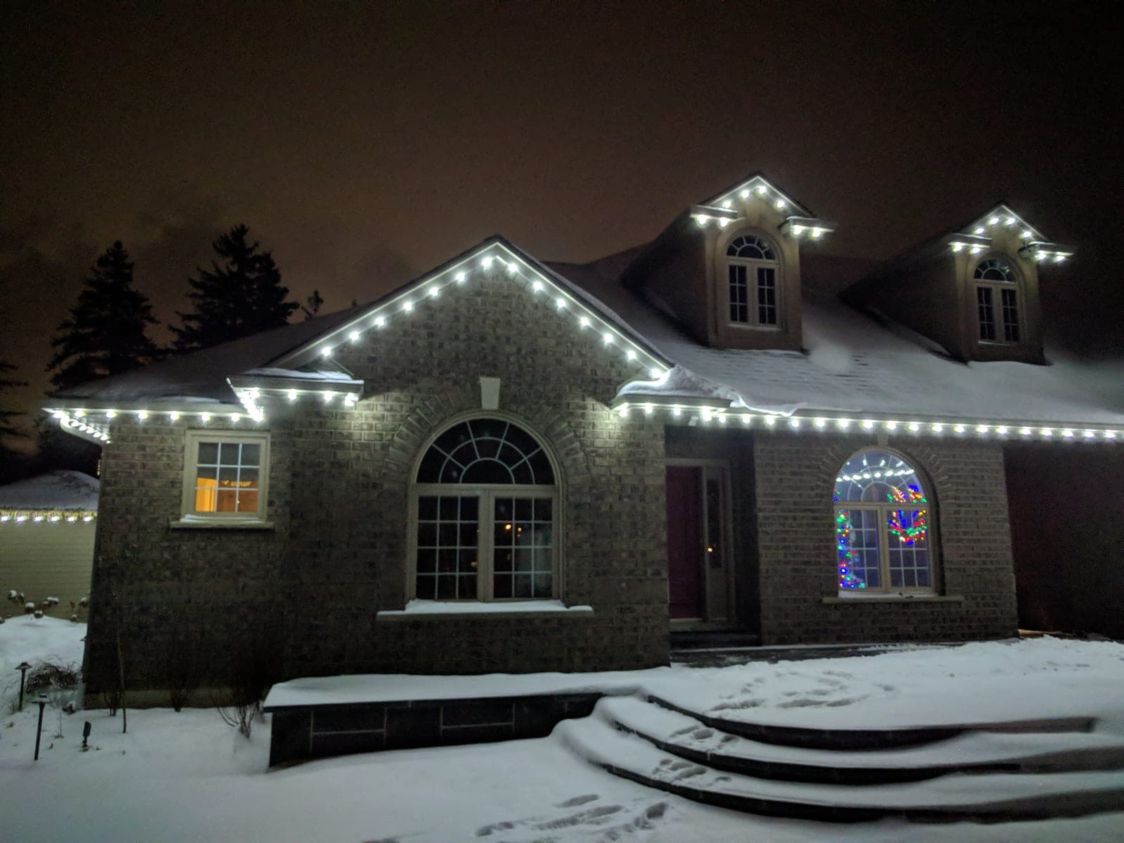 Warm white C9 lights outlining the roofline of a two-storey brick home in Hamilton, Ontario at dusk