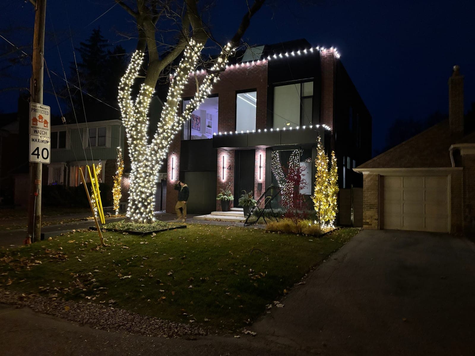 Modern brick home with a front tree wrapped in warm white lights and matching roofline outline lighting.
