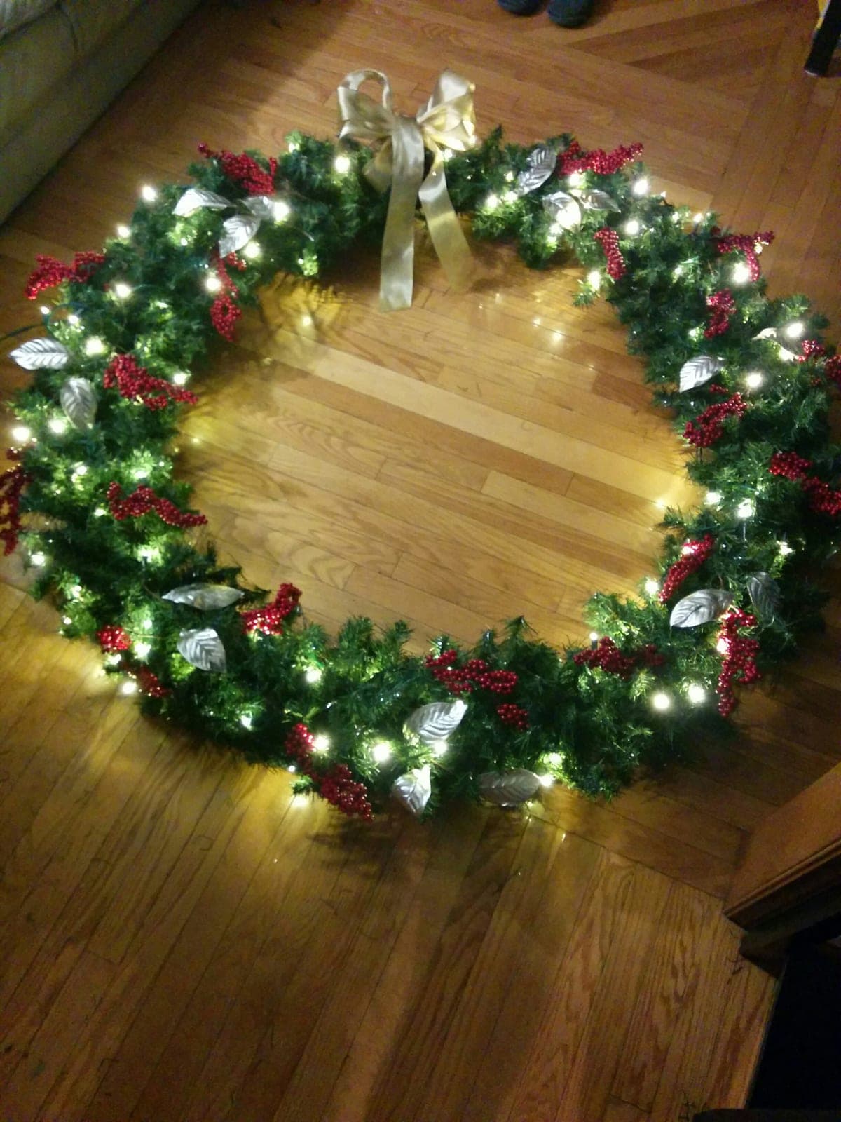Large pre-lit artificial Christmas wreath decorated with red berries, silver leaves and a gold bow.