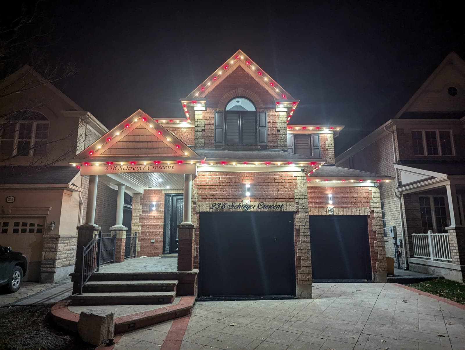 Two-storey brick home outlined in warm-white and red C9 Christmas bulbs with a lit address sign