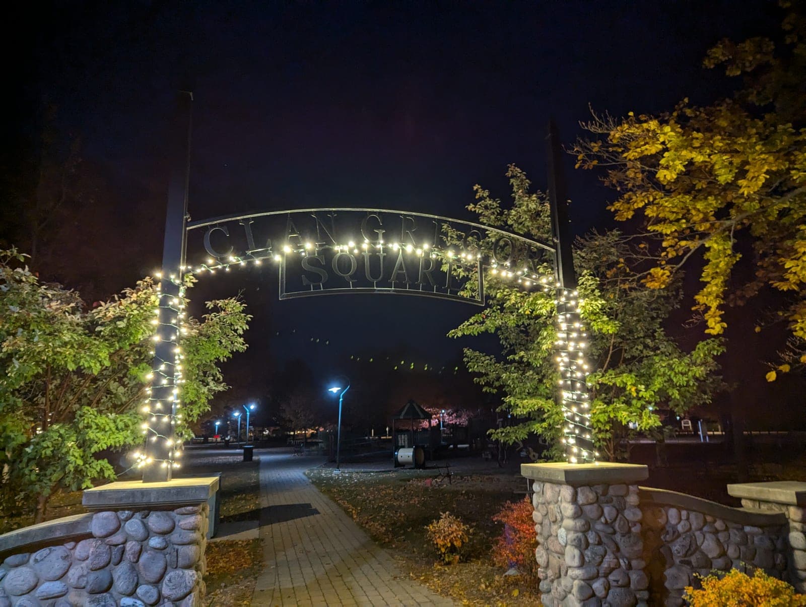 Town park entrance archway wrapped in warm-white holiday lights glowing at night